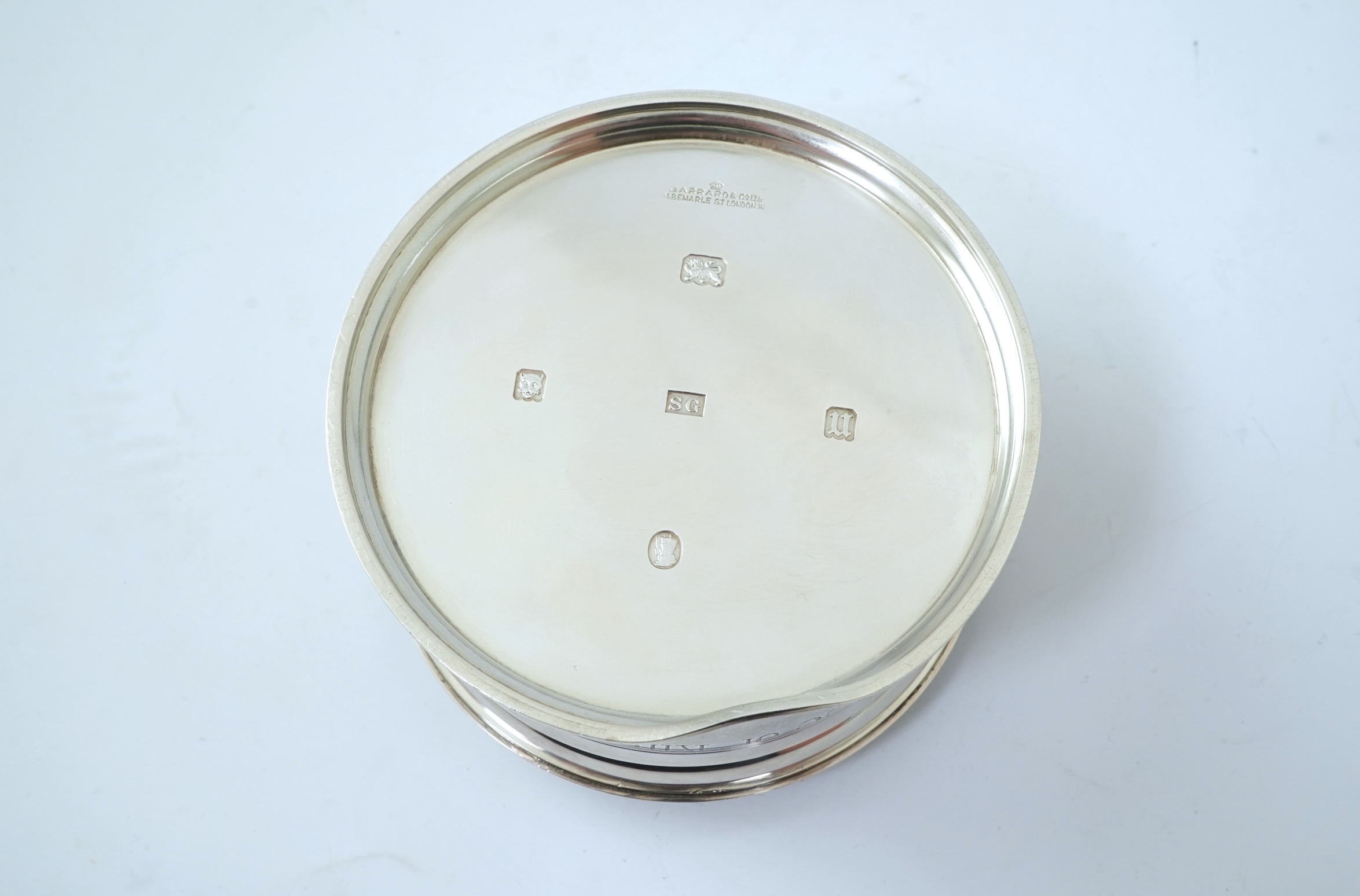 A George V silver circular inkwell, by Sebastian Garrard, commemorating the Silver Jubilee of King George V, the die stamped cover designed by George Kruger Gray featuring the Goldsmiths Company Coat of Arms